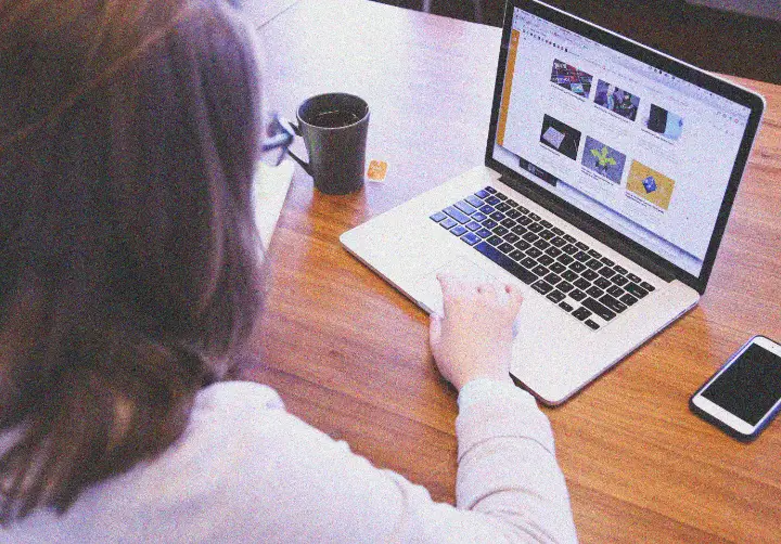 Someone browsing a website on a laptop at a wooden desk.